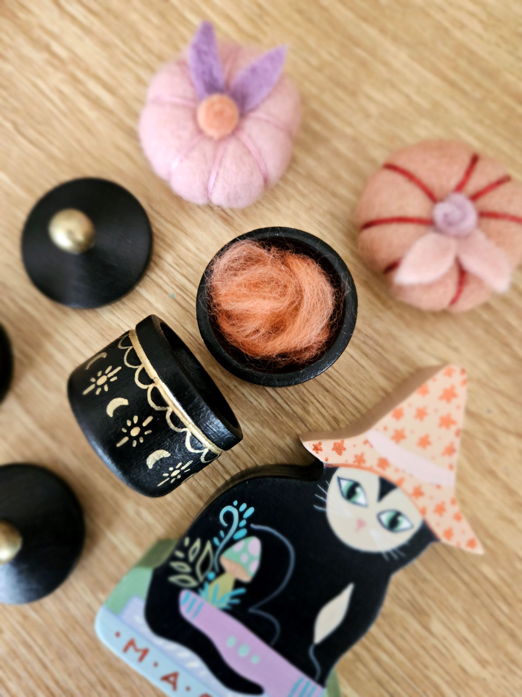 A collection of wooden witchcraft items including a cauldron with a removable lid, a witch's hat, and a witch's dress. All items are hand-painted with various designs including moons and stars.