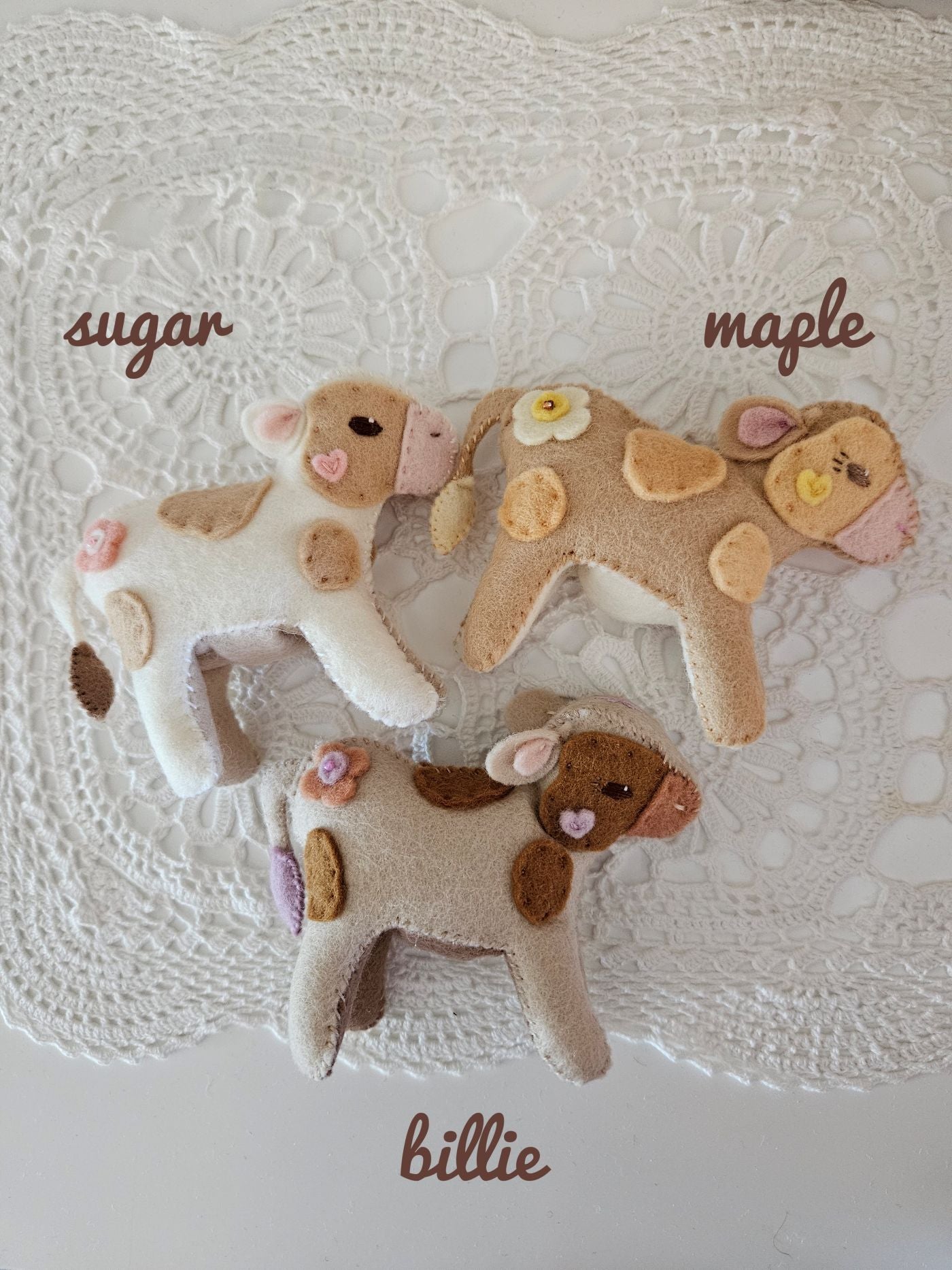 Three felt cow toys labeled 'sugar', 'maple', and 'billie' on a textured white background.