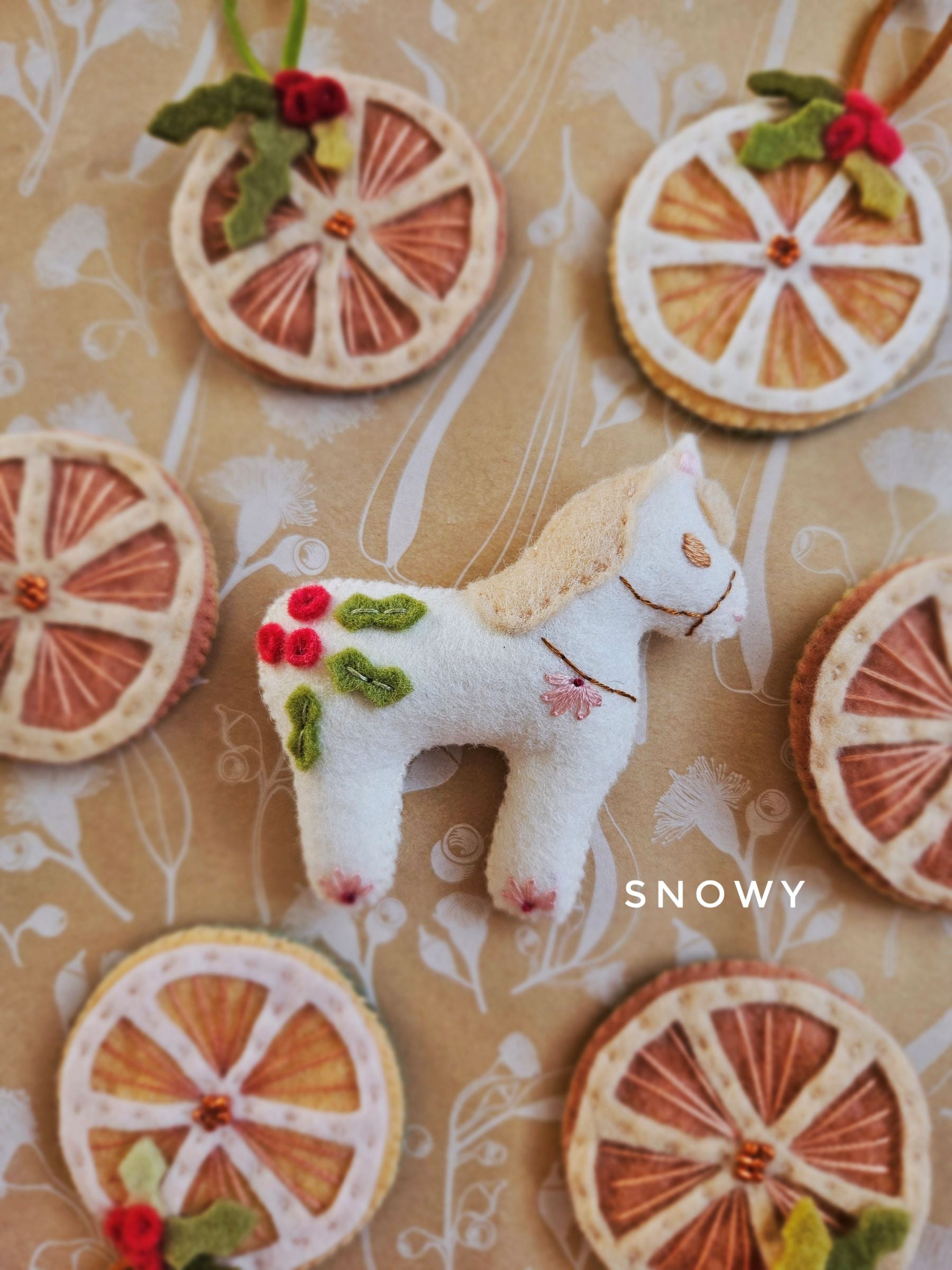 Decorative arrangement with a white horse figure and orange slices on a patterned background, featuring the brand 'SNOWY'.