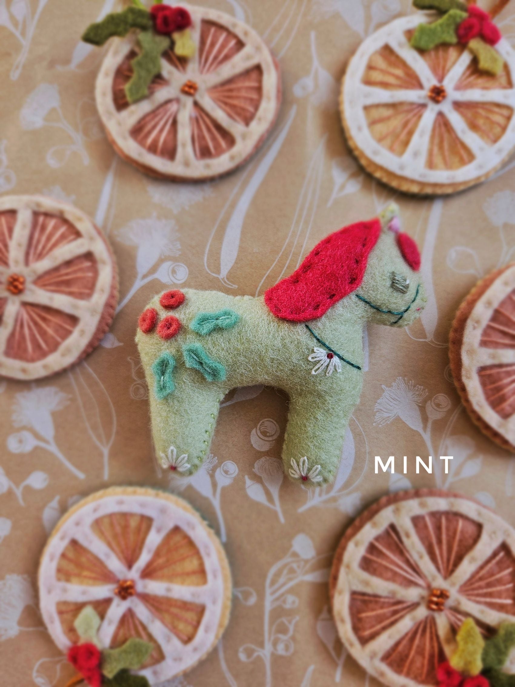 Felt toy horse with floral details on a patterned background with 'MINT' branding.