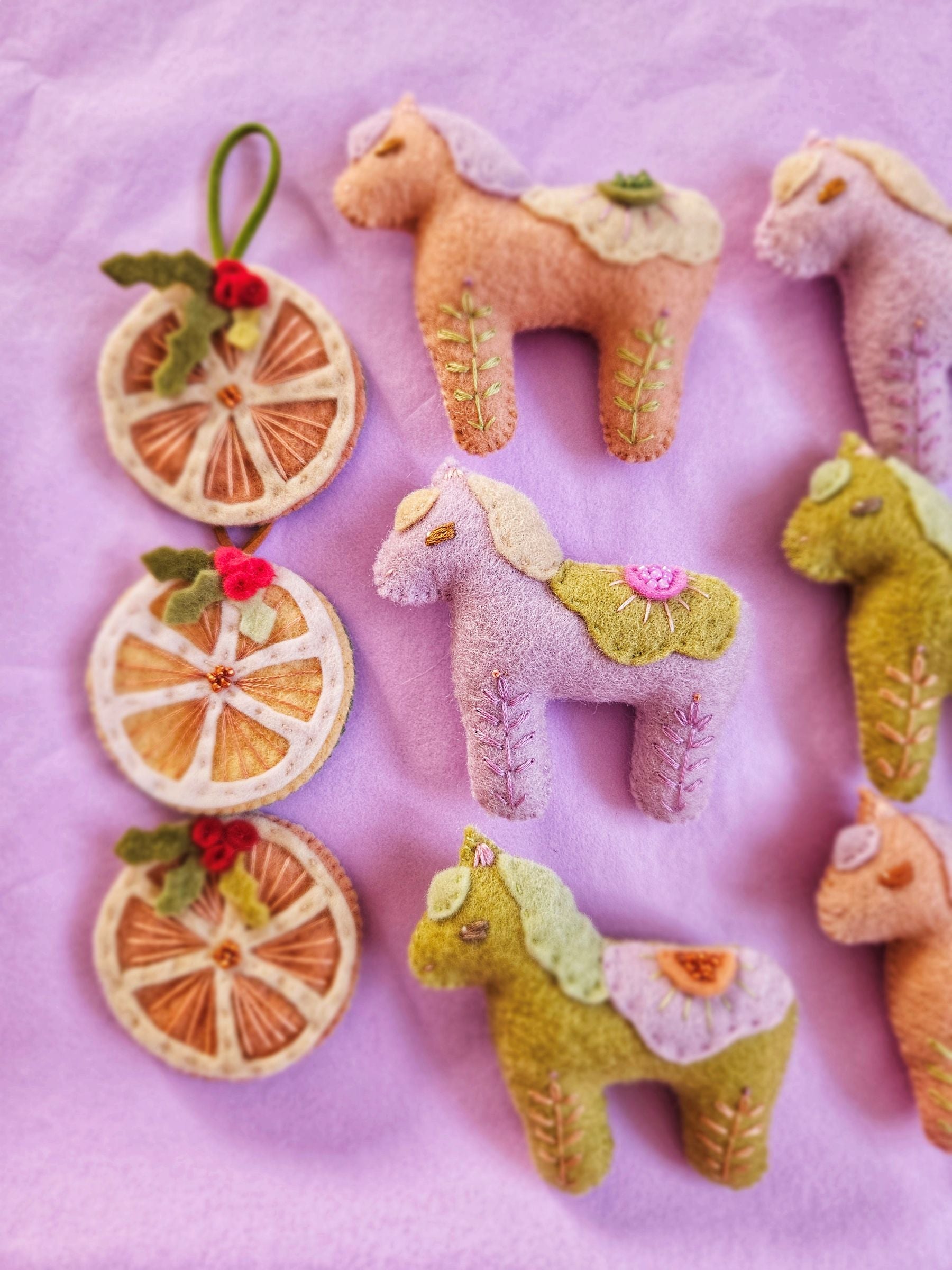 Felt horse toys and decorative citrus slices on a pink background