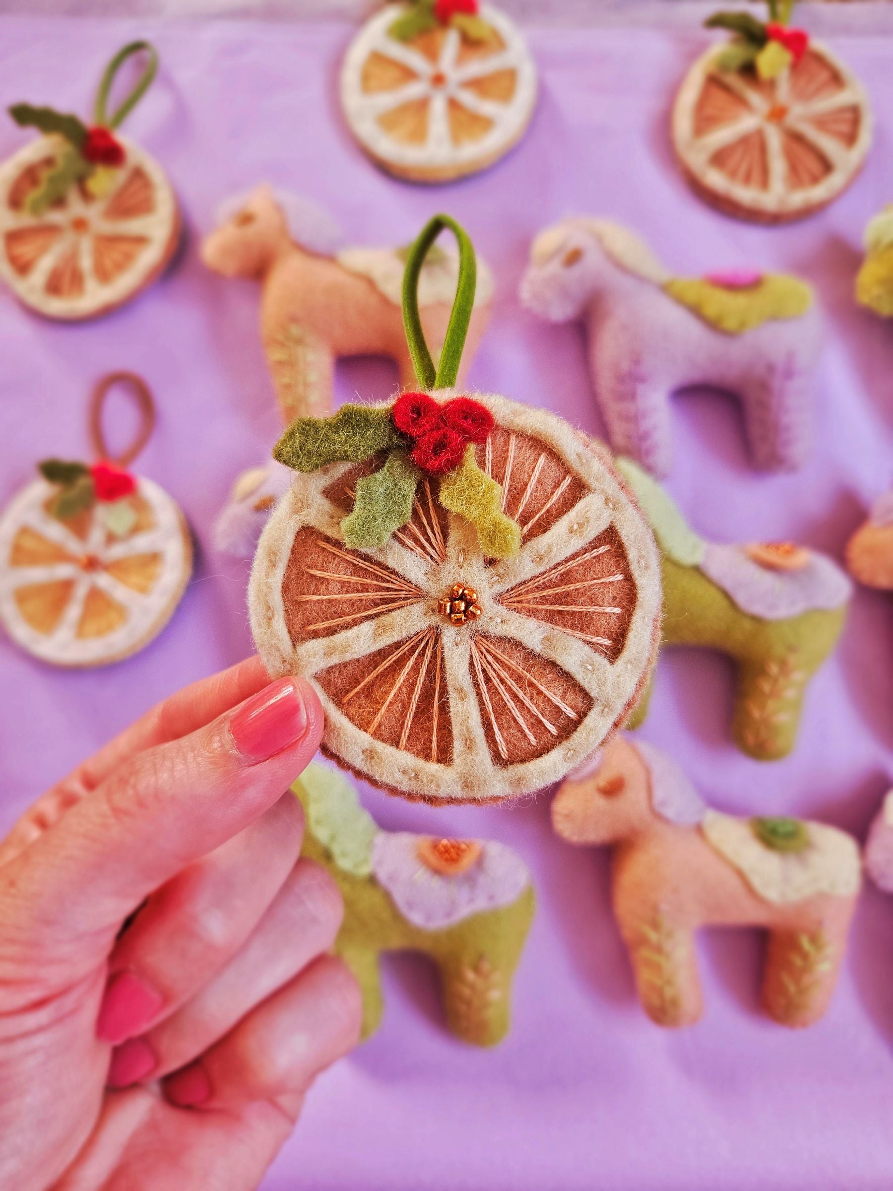 Decorative wheel ornament held by a hand with colorful felt animals in the background on a purple surface.