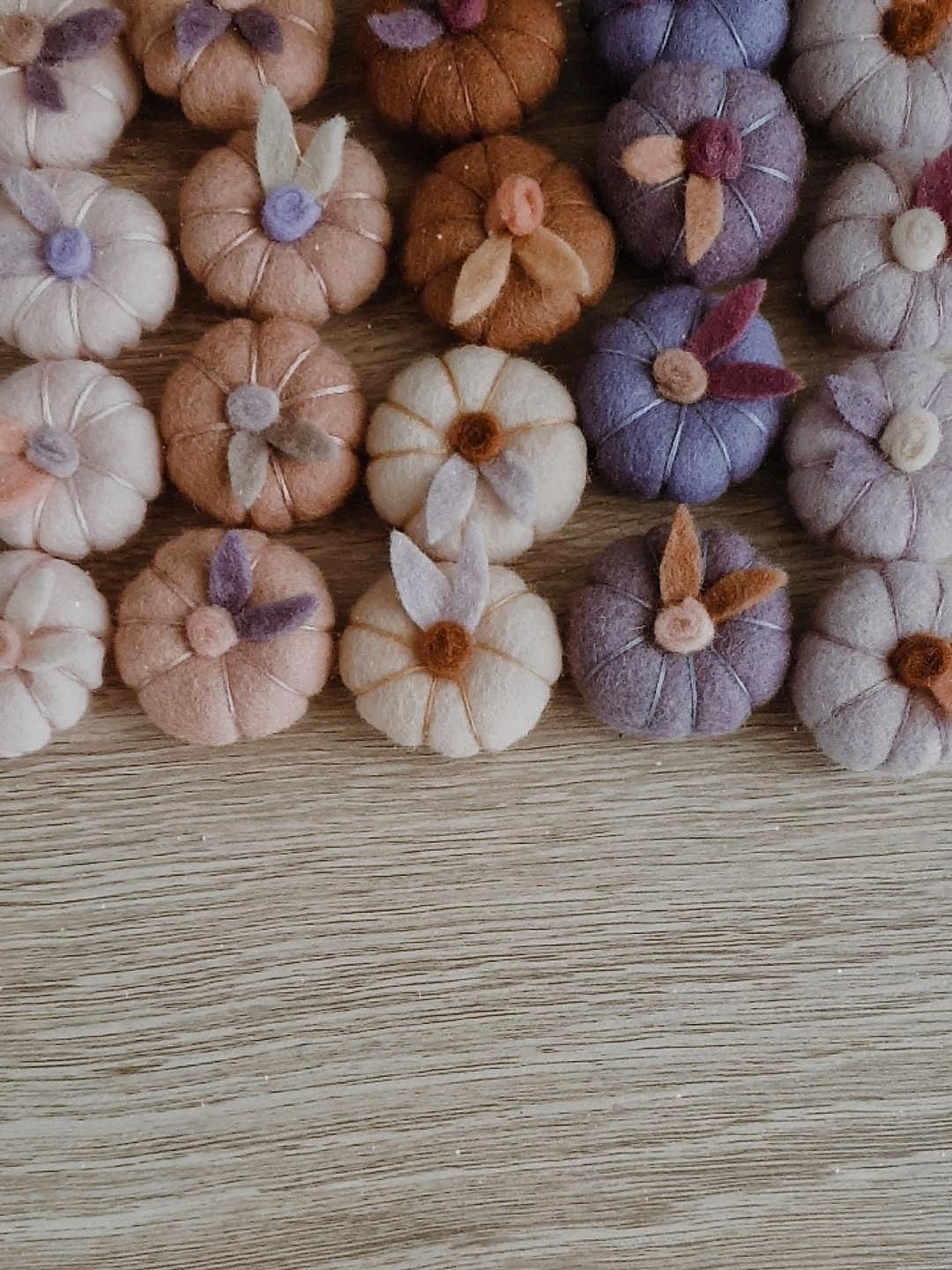 A collection of handmade wool felt pumpkins in various shades, displayed on a textured background.