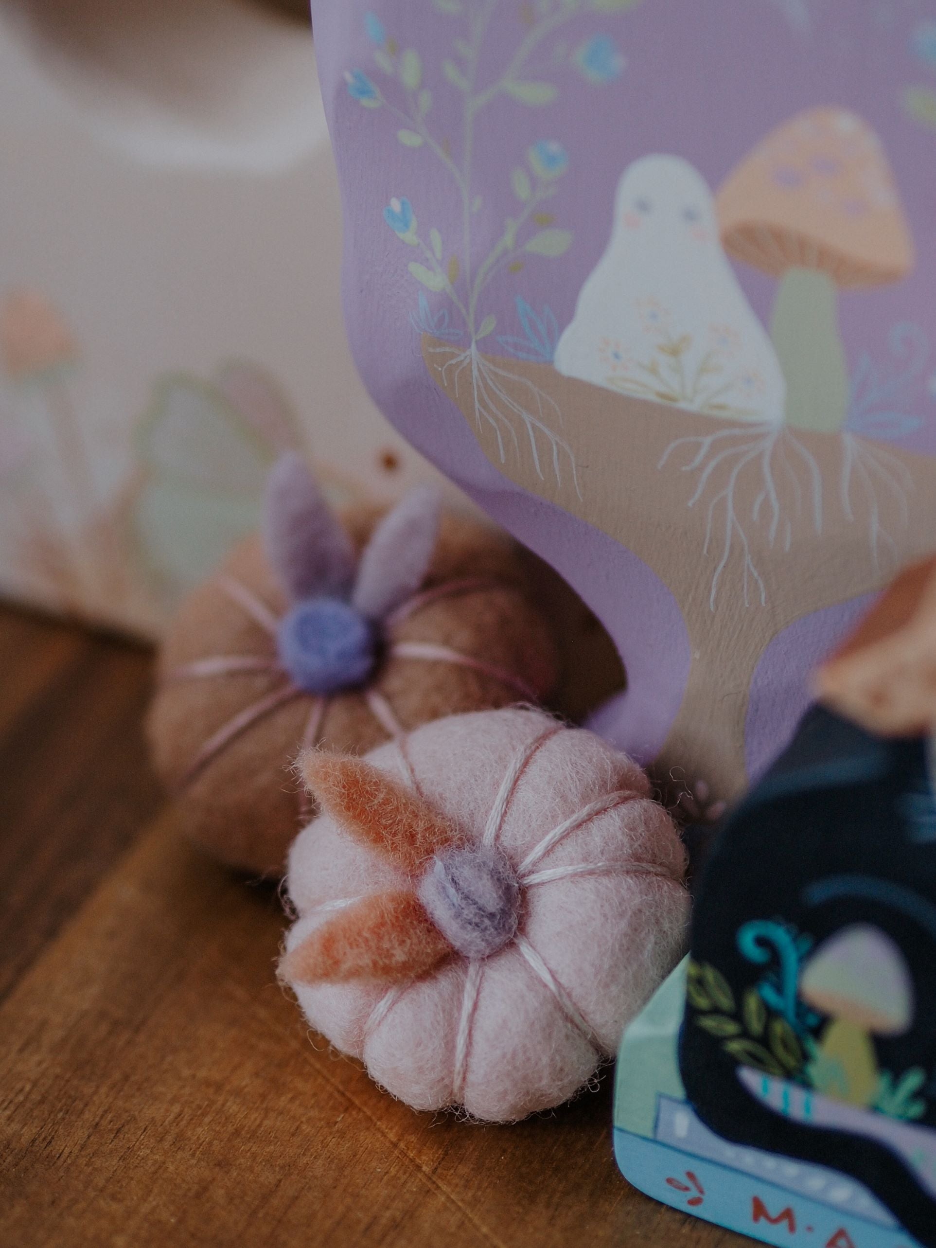 Small felt pumpkins with a decorative card featuring mushrooms on a wooden surface