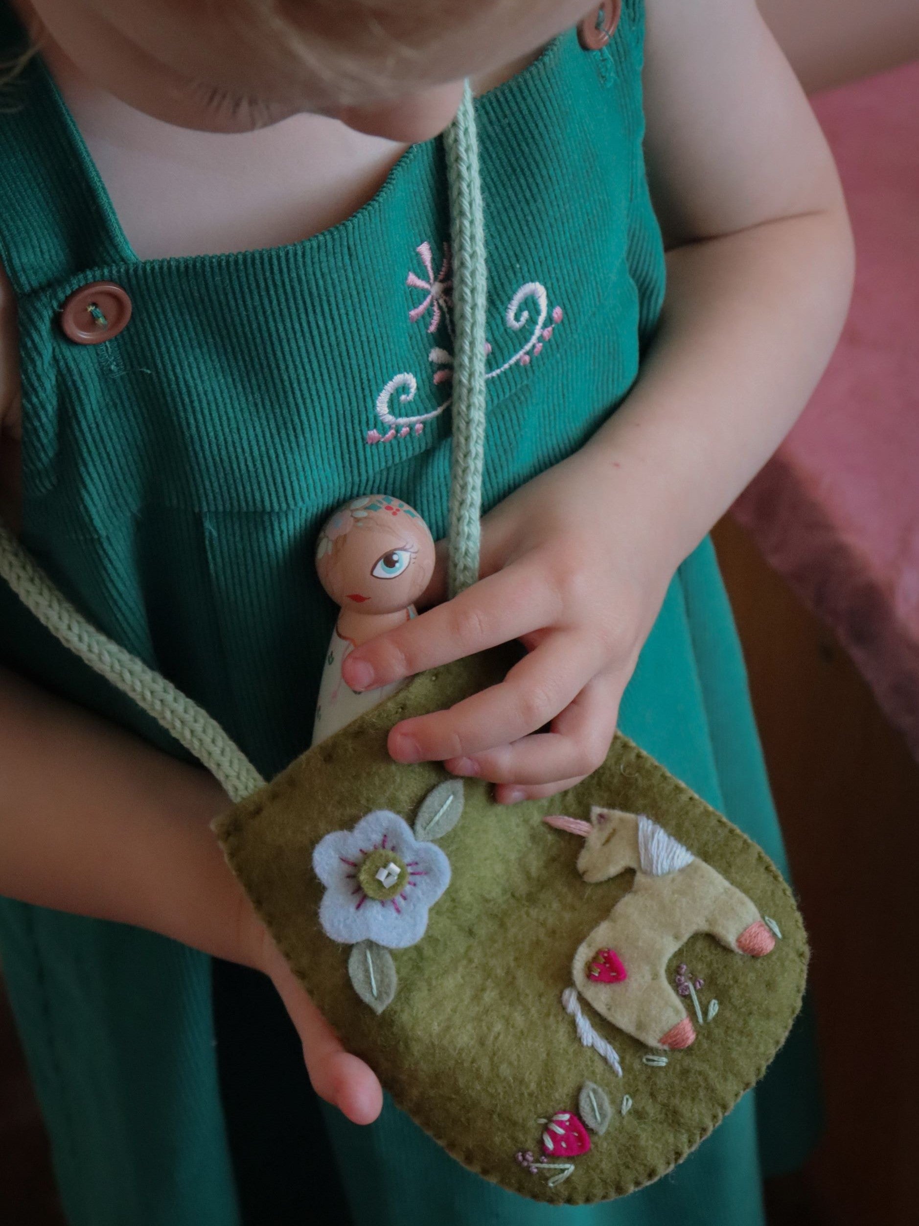 A child holding a green handcrafted felt bag with an embroidered flower and an animal design.