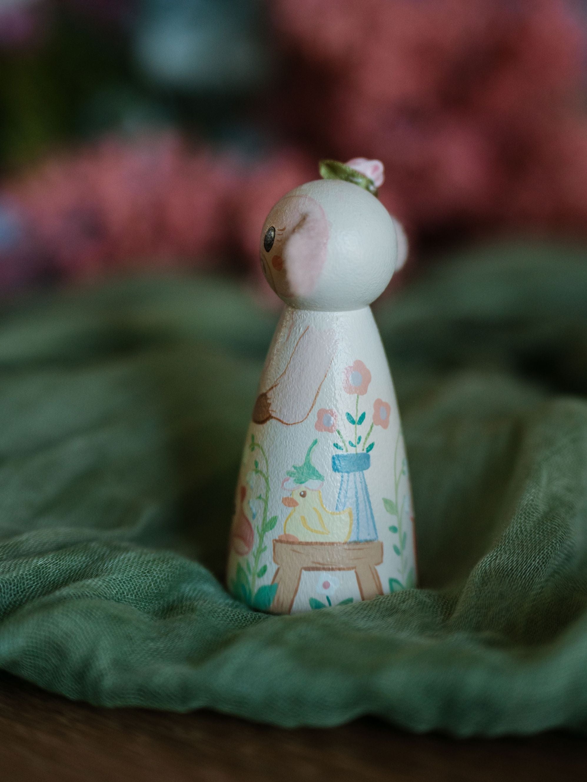 Decorative wooden peg doll with floral design on a green fabric background