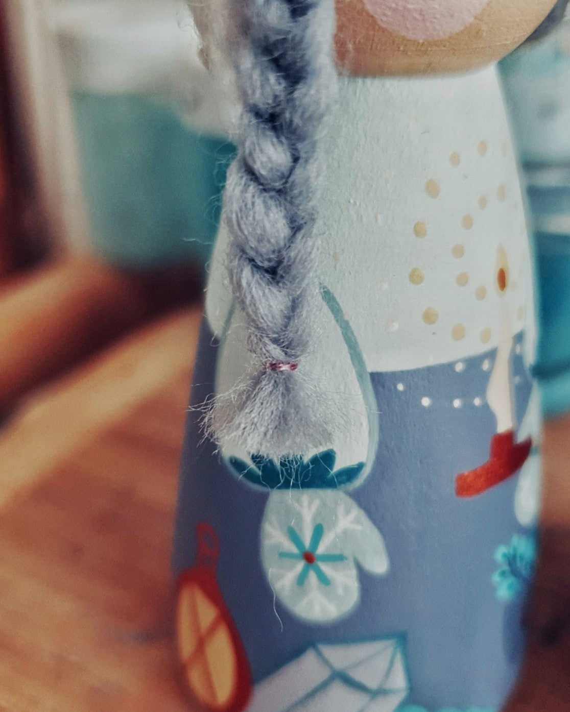 Close-up of a wooden toy with a braided hair detail, wearing a blue outfit with floral patterns.