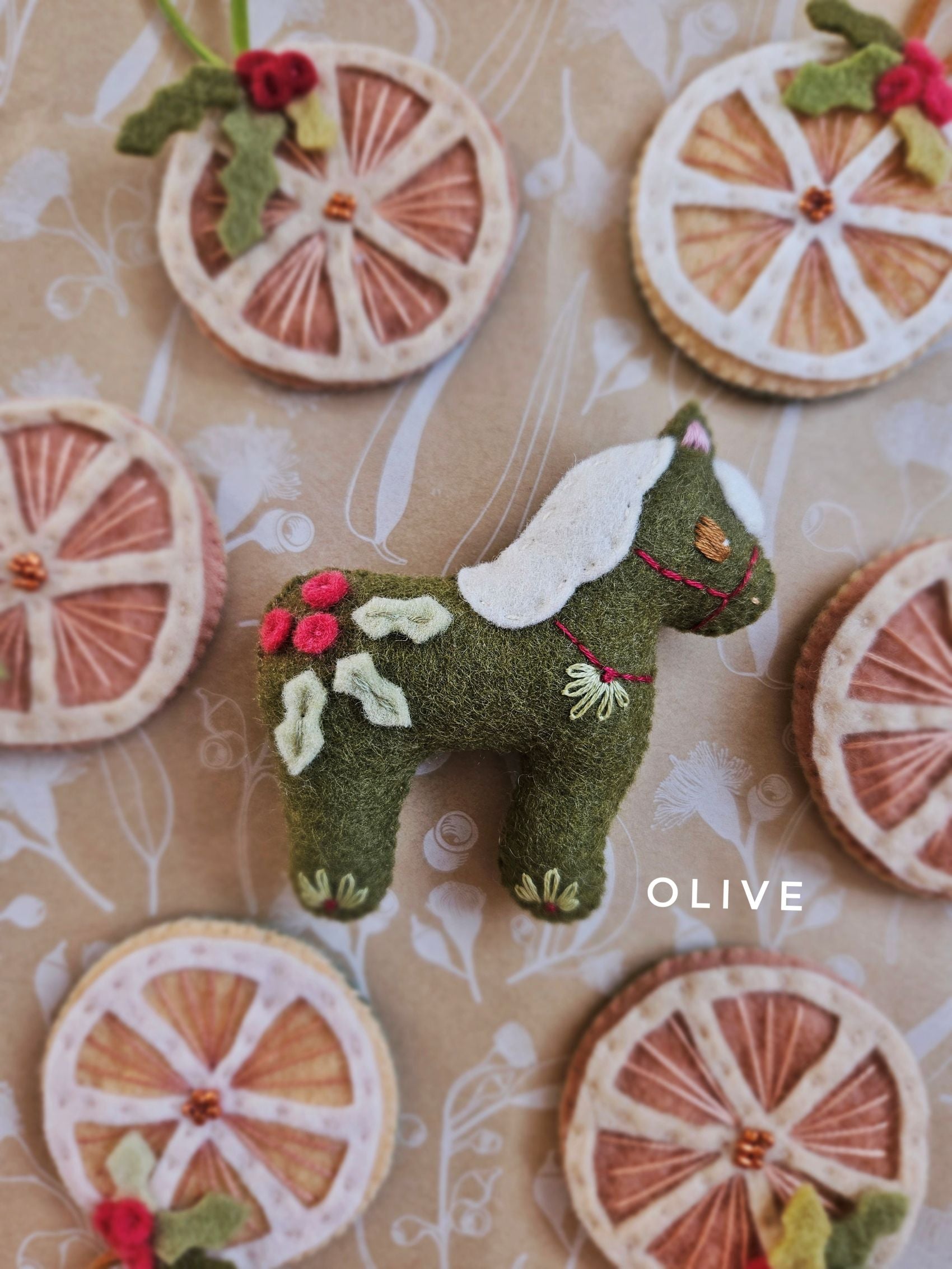Green felt horse toy with floral details on a patterned background