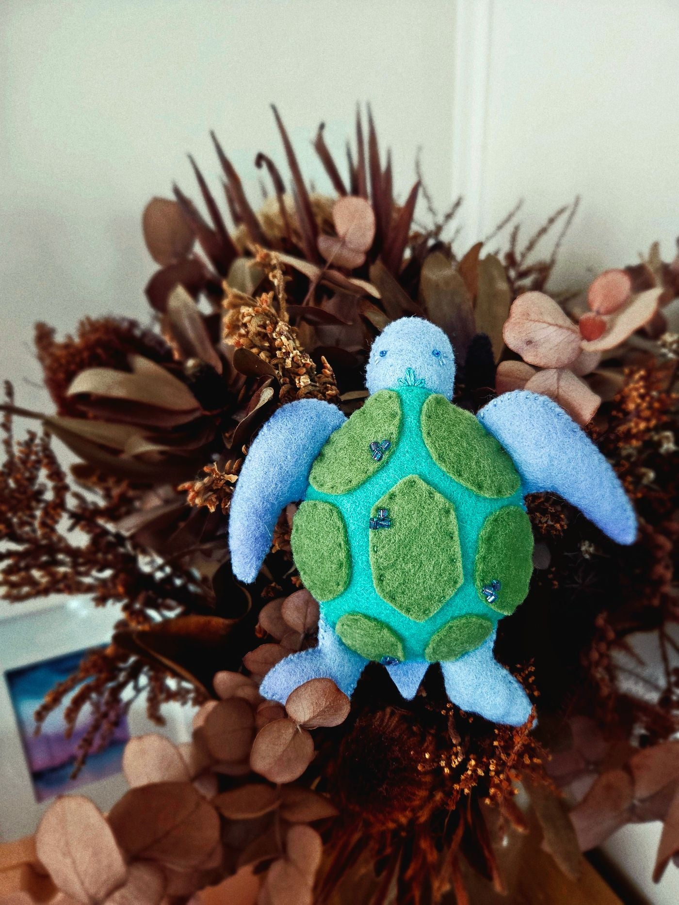 Plush turtle toy on a decorative wreath with foliage and flowers.