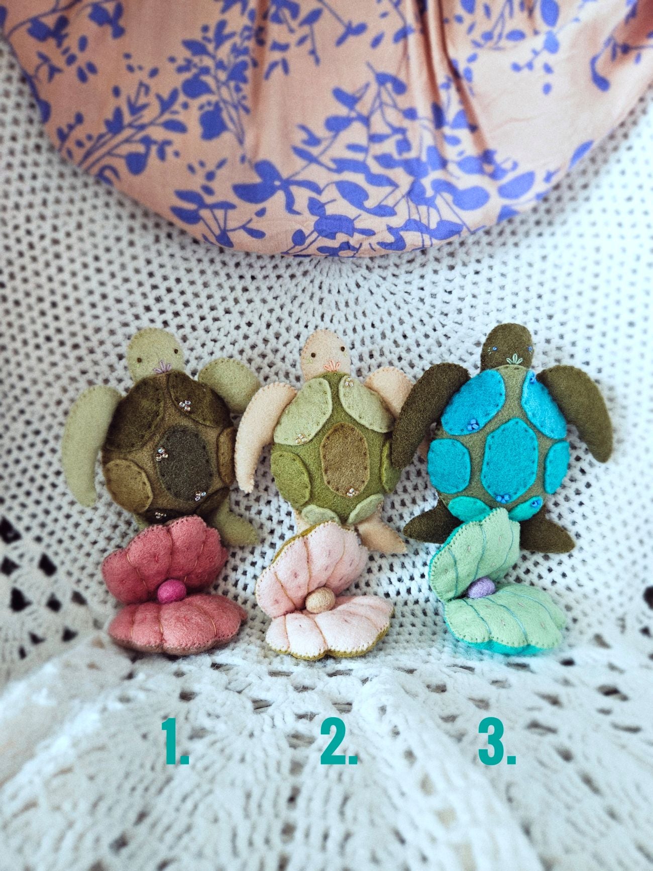 Three colorful turtle-shaped hair accessories on a textured surface with a floral-patterned fabric in the background.