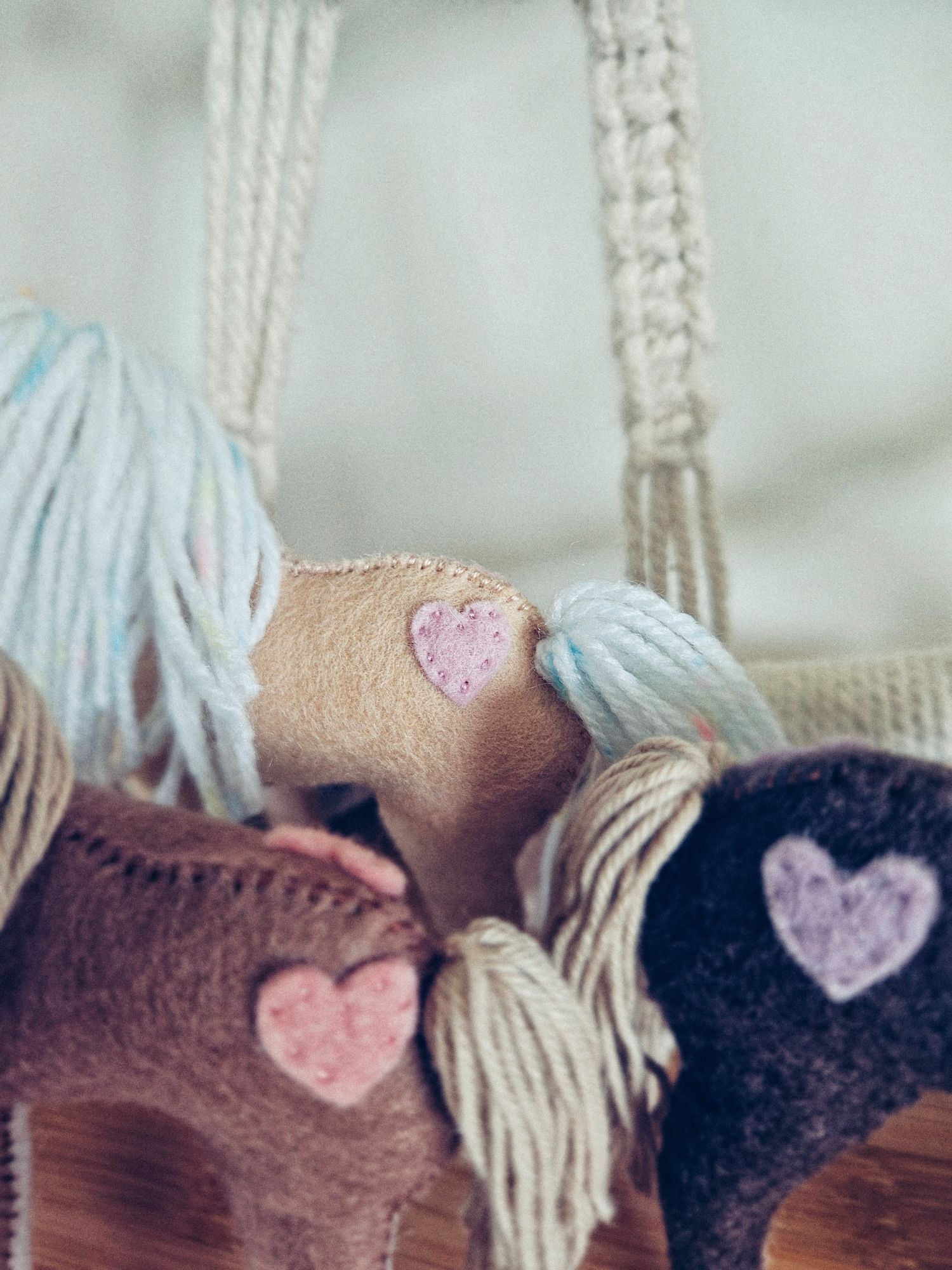Knitted felt items with heart patterns hanging on a macrame wall hanging.