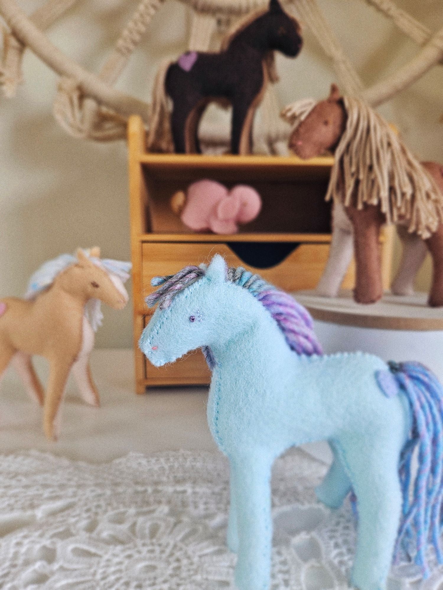 Collection of toy horses in a room setting with a wooden shelf.