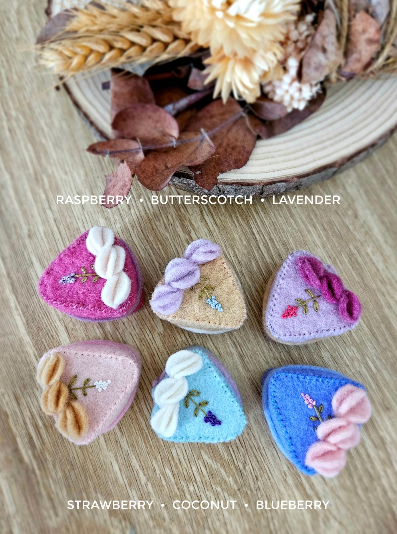 Set of lavender themed felt cake slices with embroidery, in various colors on a wooden surface with dried flowers in the background.