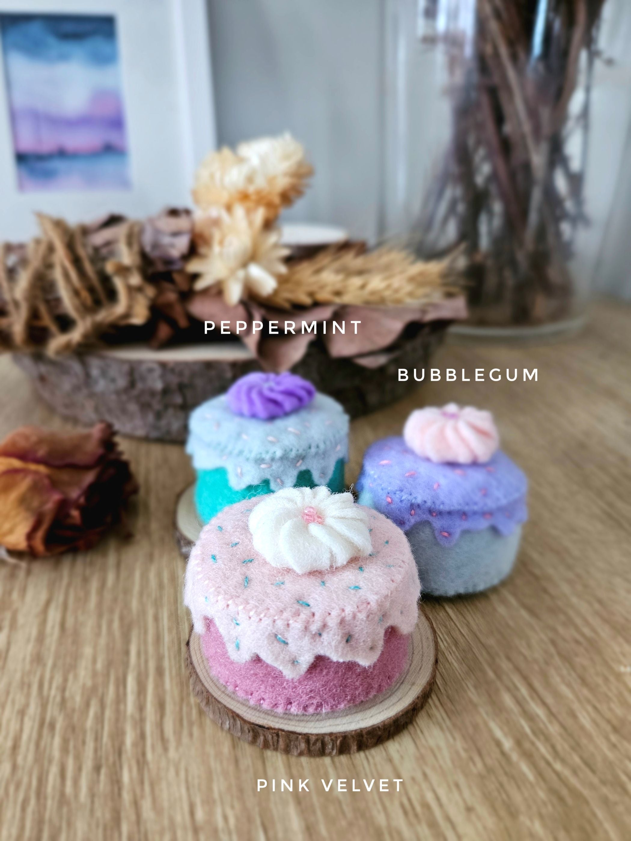 Three small felt cupcakes labeled 'Peppermint', 'Bubblegum', and 'Pink Velvet' on a wooden surface.
