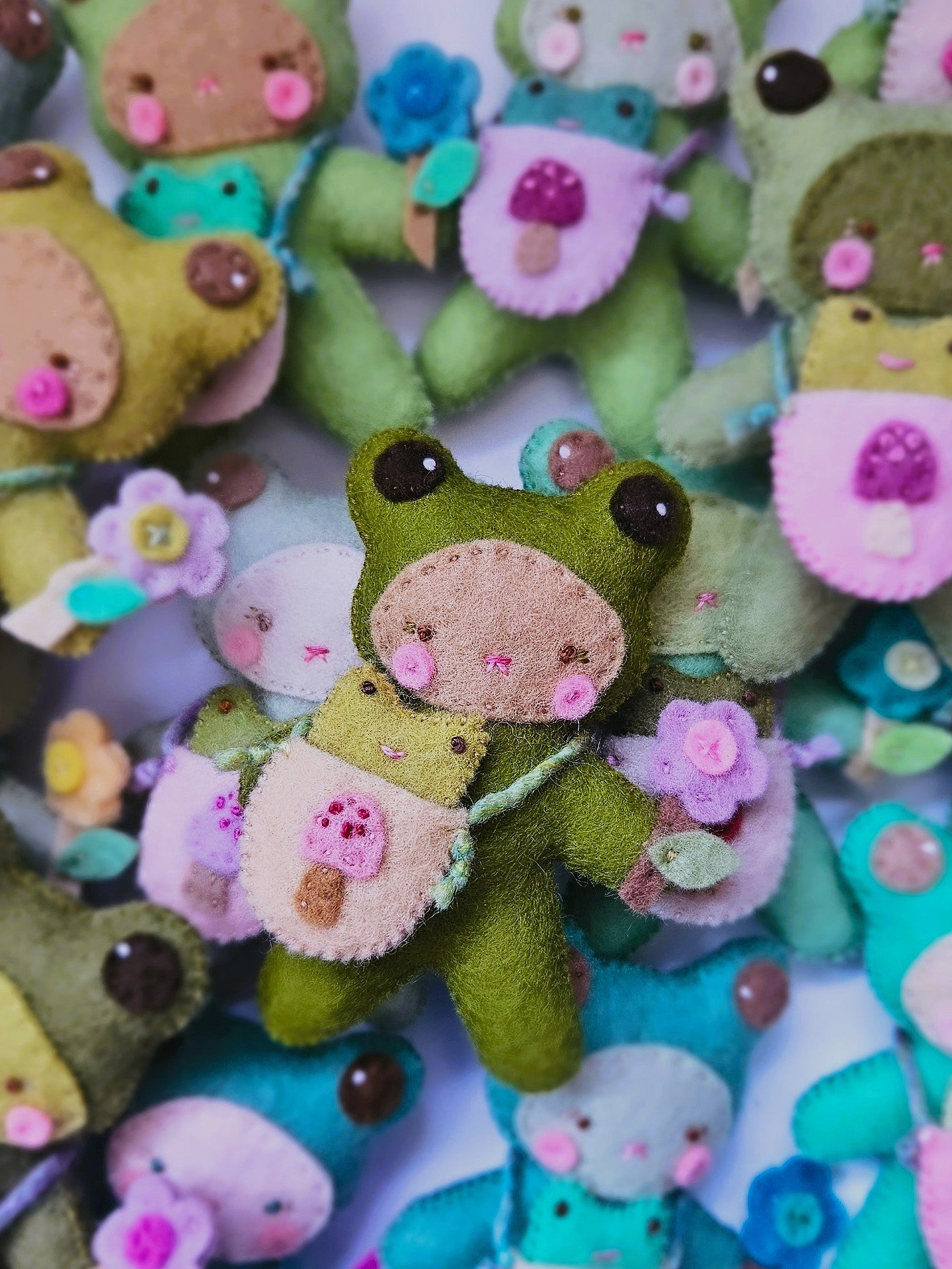 Collection of colorful felt toys with frog designs on a white background
